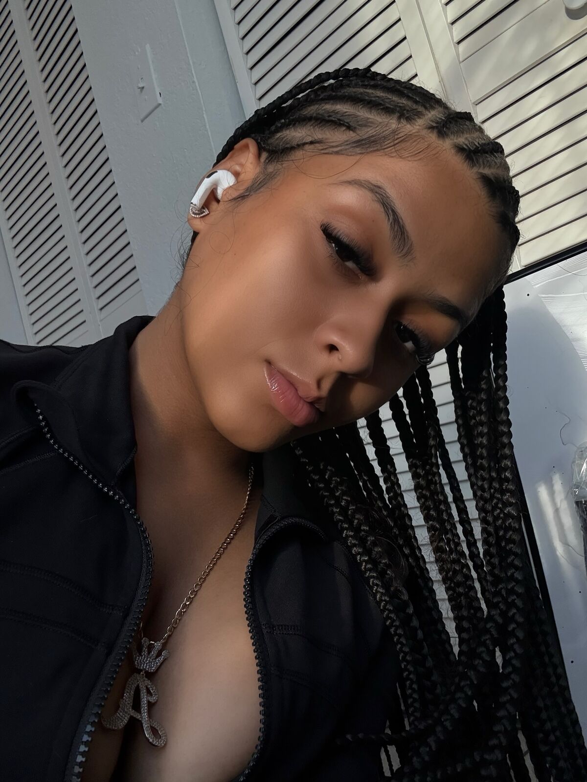Selfie of LA Real Ash with long braids, black zip-up jacket and white earbud
